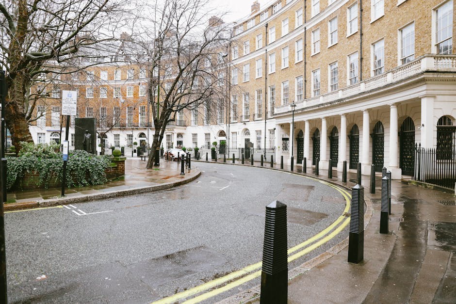 A street scene in Belgravia featuring a row of elegant white Victorian-style buildings with ornate architectural details, large sash windows, and decorative moldings. The buildings have small balconie
