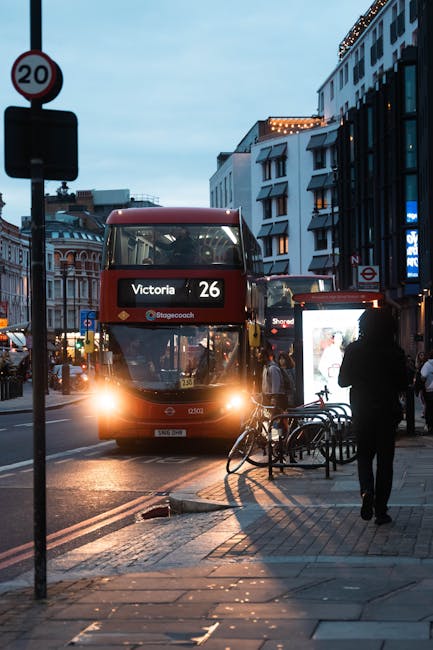 A red double-decker bus with route number 26 and destination Victoria is approaching a busy street in Belgravia during early evening, with streetlights and building lights starting to illuminate the u